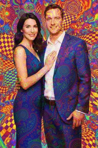 AI-generált szelfi egy mosolygó párról, pszichedelikus stílusban. Élénk, vibráló színek, örvénylő minták, fraktálok és torzult formák kavarognak a háttérben és a szereplők körül. A kép hallucinogén, álomszerű hangulatot áraszt.