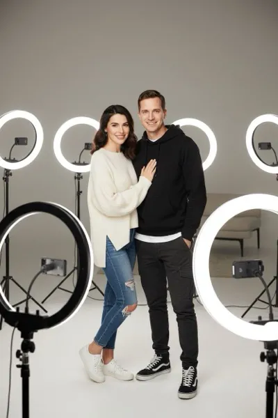 AI-generált portré egy mosolygó párról, akik modern, stílusos környezetben, okostelefonnal és ring light lámpával pózolnak. Háttérben esztétikus dekoráció és követők számát mutató képernyő látható.